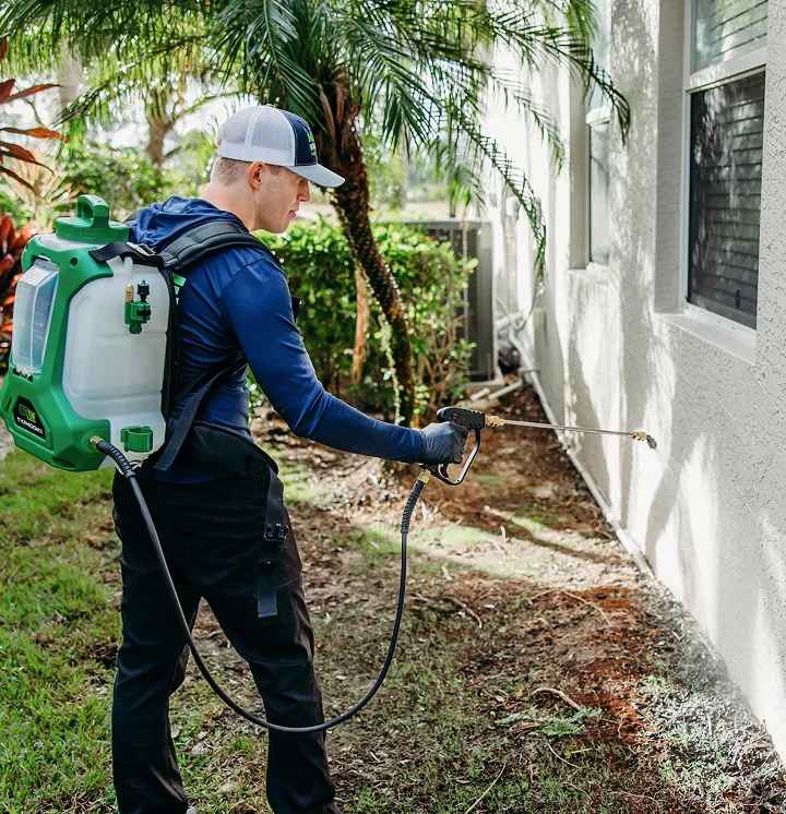 Pest control technician applying ant treatment to the exterior of a home
