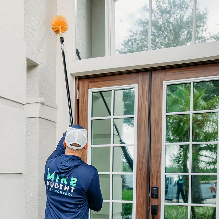 Mike Nugent pest control technician removing spider webs from a home exterior