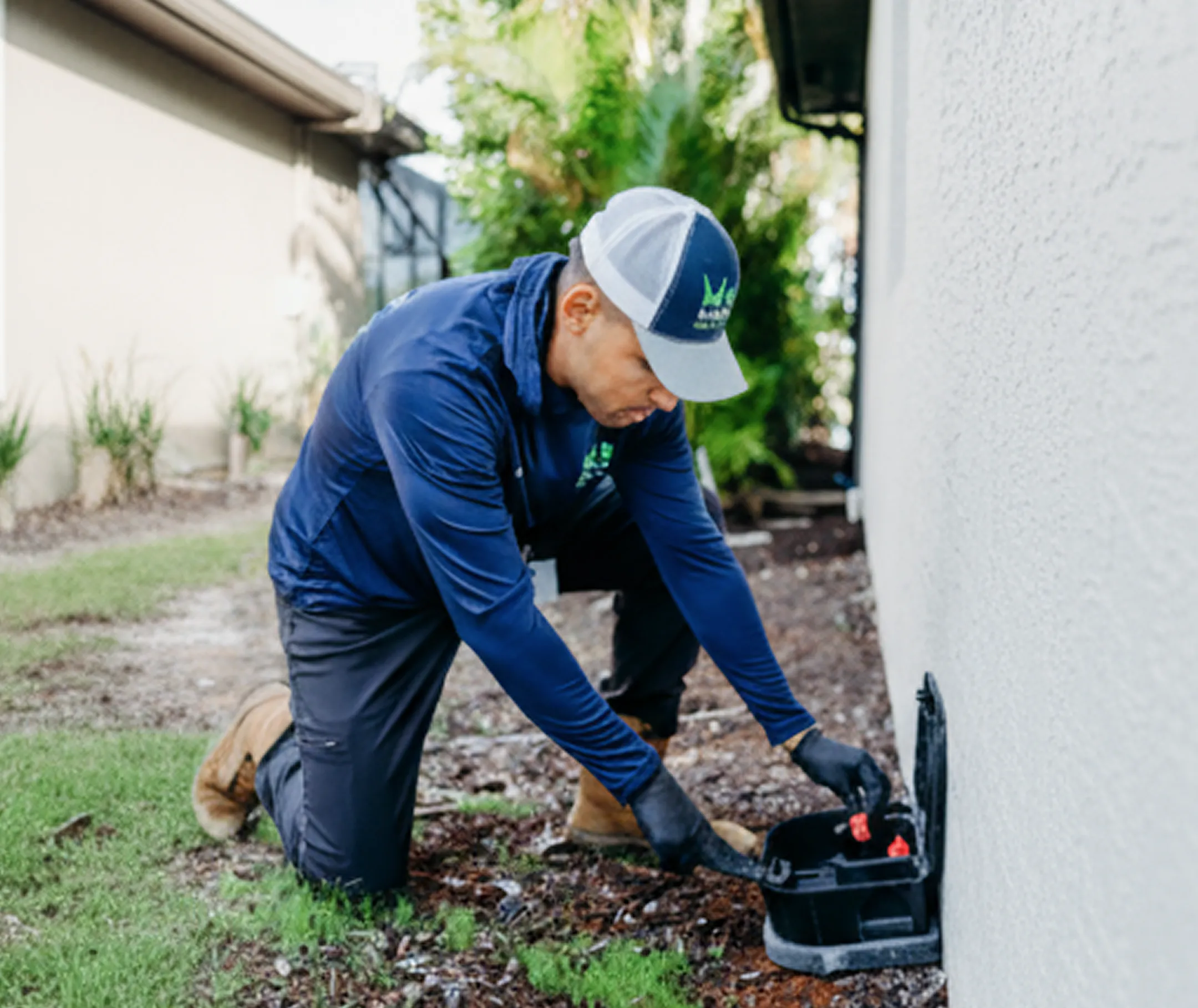 Pest control technician placing a rodent bait station outside a residential home