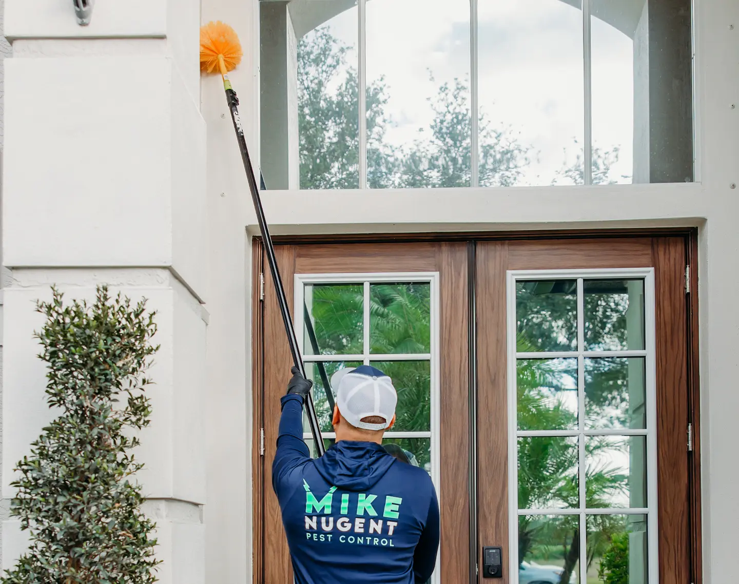 Man in pest control uniform holding large stick above doorframe